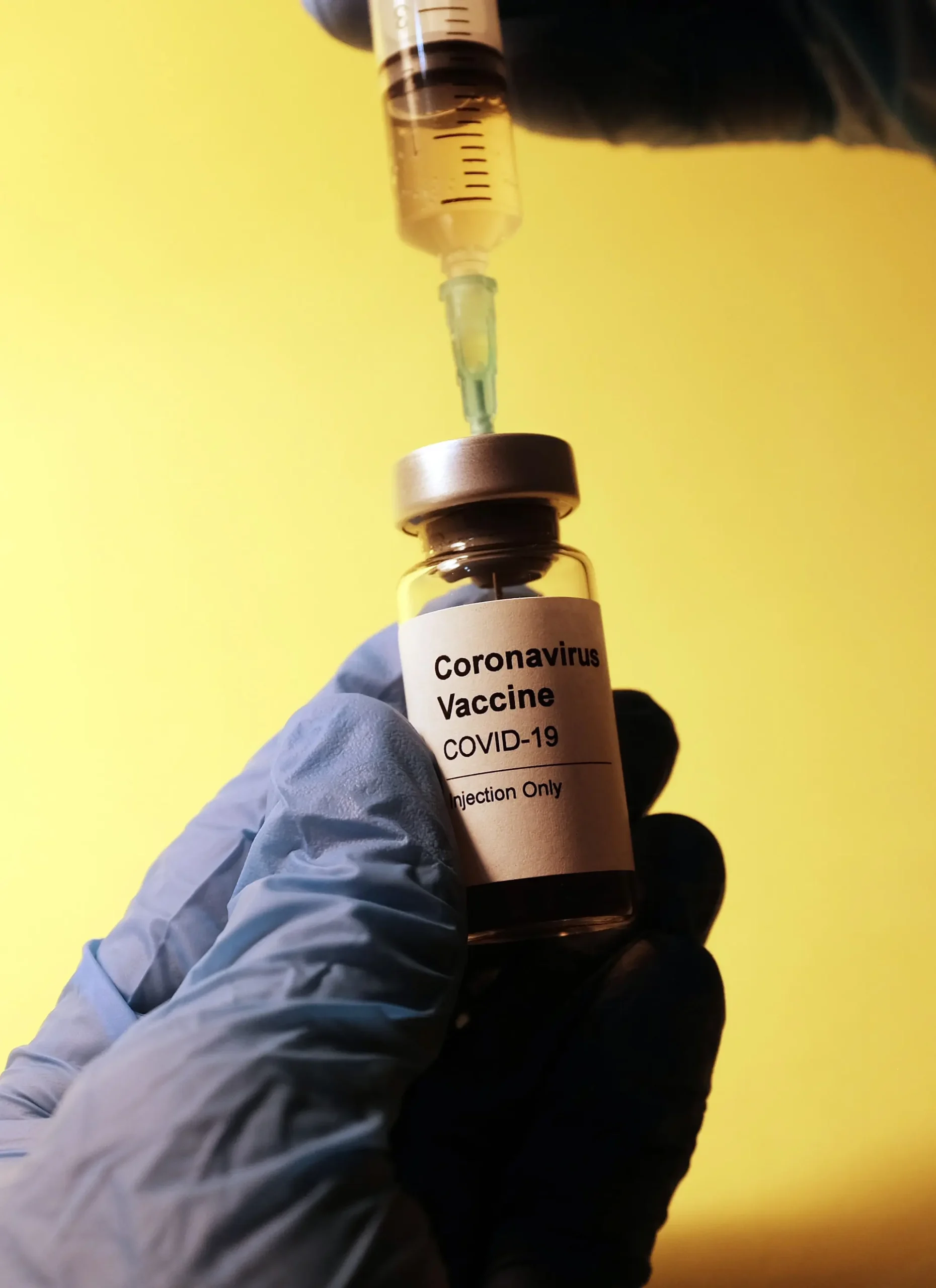 Close up of surgical gloved hand holding COVID-19 vaccine phial