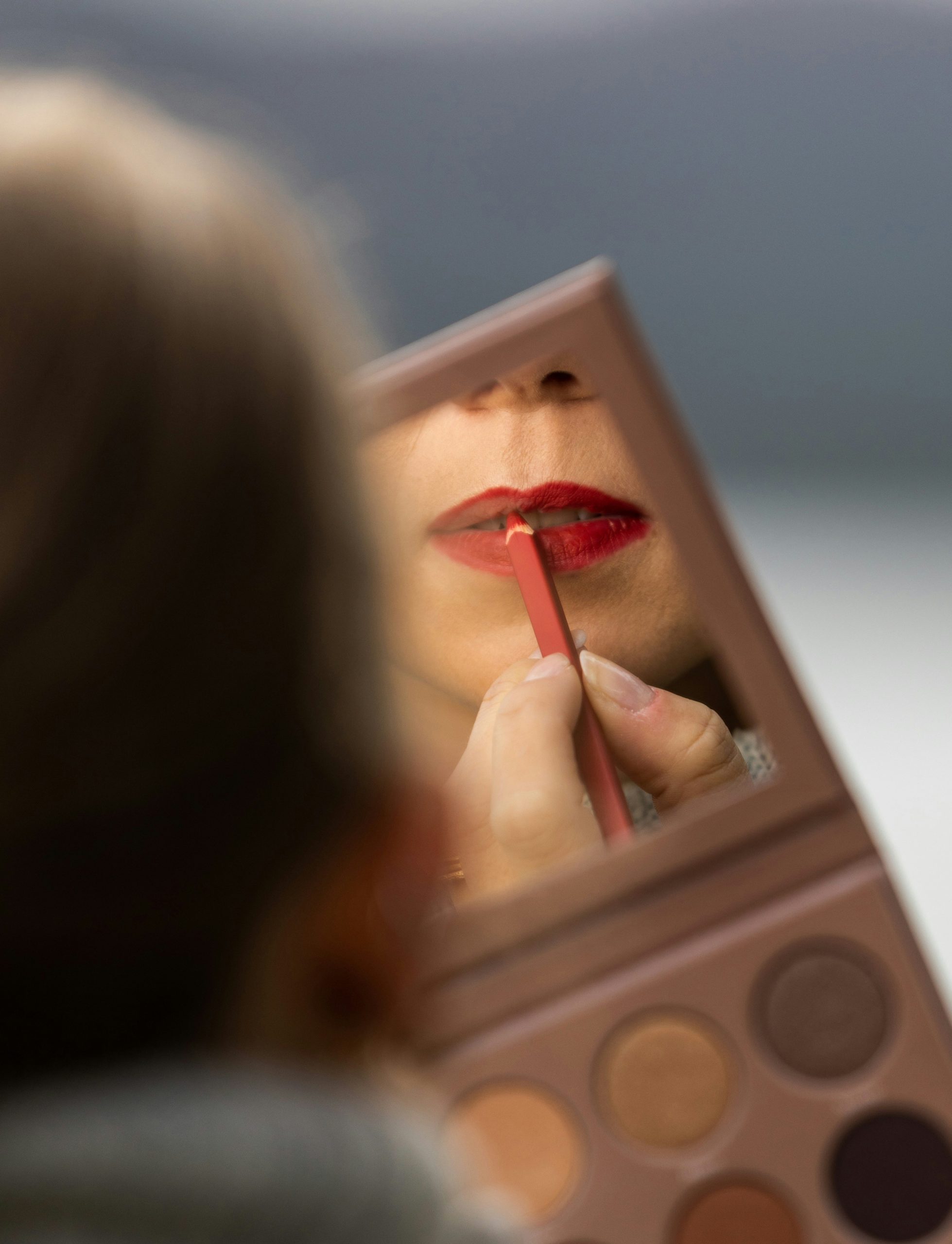 Close-up of person looking in a mirror applying lipstick